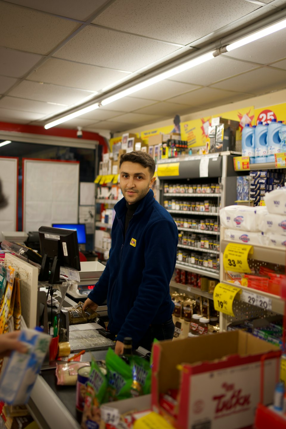 Man smiles while scanning groceries at a small store counter.