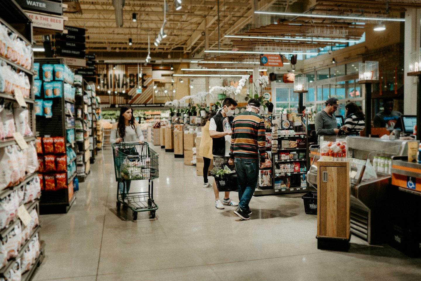 Shoppers in a modern grocery store with masked man talking to someone.